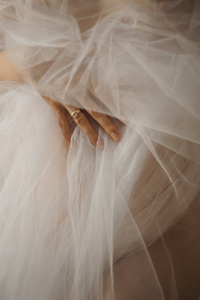 A close-up image of a delicate hand adorned with a ring, gracefully touching elegant tulle fabric.