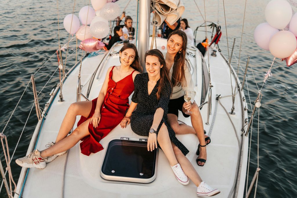 Three women celebrate on a yacht at sunset, enjoying a cheerful and memorable time.